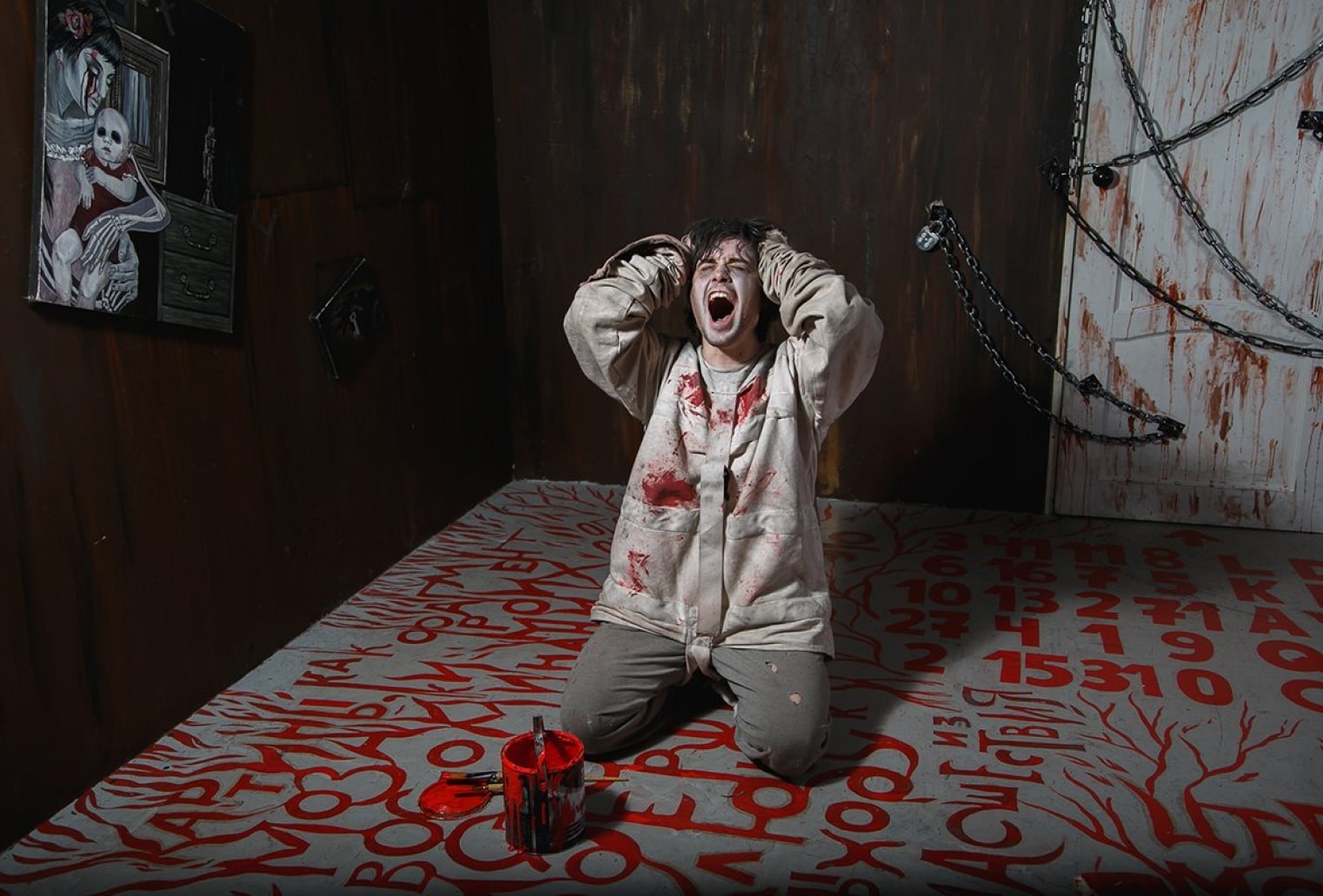 Man in a bloody straightjacket screaming inside an escape room puzzle.