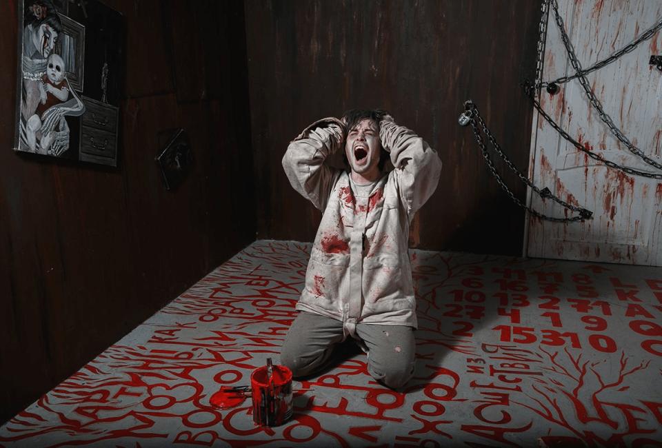 Main in a bloody straightjacket screaming inside an escape room puzzle.